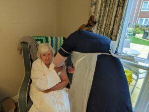 Image shows an elderly lady receiving her Covid-19 Autumn booster injection from a nurse