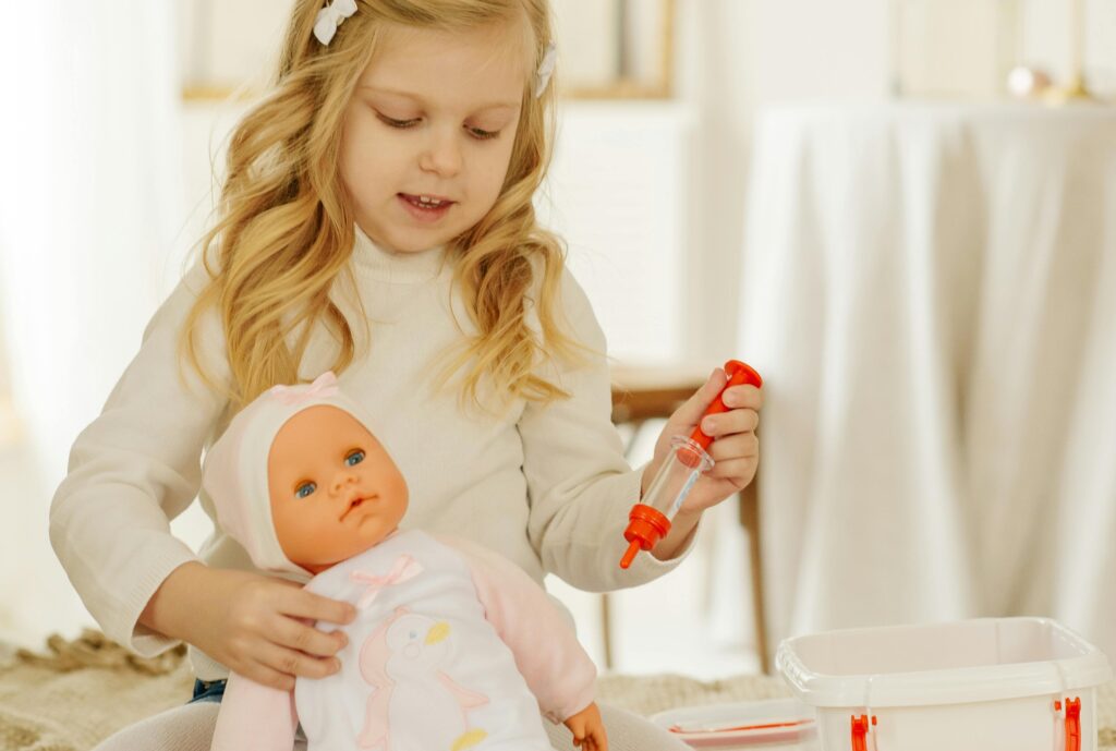 Child playing with plastic medical injection and a baby dolly