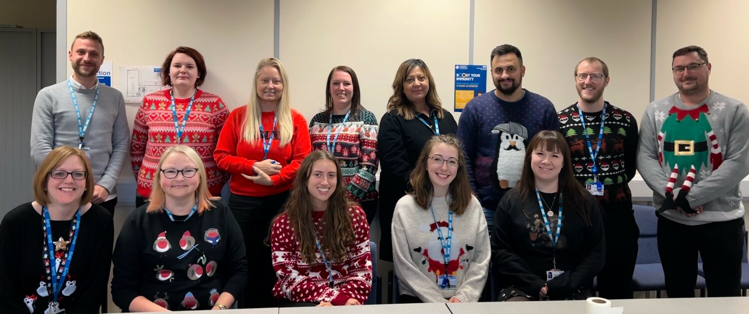 Image shows a group of people together wearing Christmas jumpers